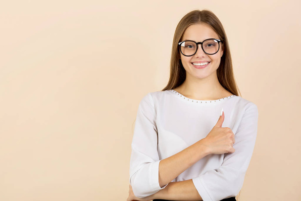 beautiful young woman in glasses on beige background with hand gesture - Foto, afbeelding