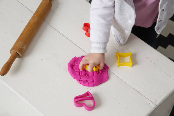 Kleinkind spielt mit Knetmasse. Spielteig ermöglicht es den Kindern, Feinmotorik zu entwickeln, Finger, Hände und Handgelenke zu stärken, von Natur aus neugierig zu sein und die Welt mit ihren Sinnen zu erkunden. - Foto, Bild