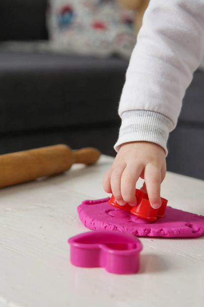 幼児の女の子は粘土のモデリングで遊んでいる。遊びの生地を使用すると、子供たちは優れた運動能力を開発し、指、手、手首を強化し、自然に好奇心と感覚を使用して世界を探索することができます - 写真・画像