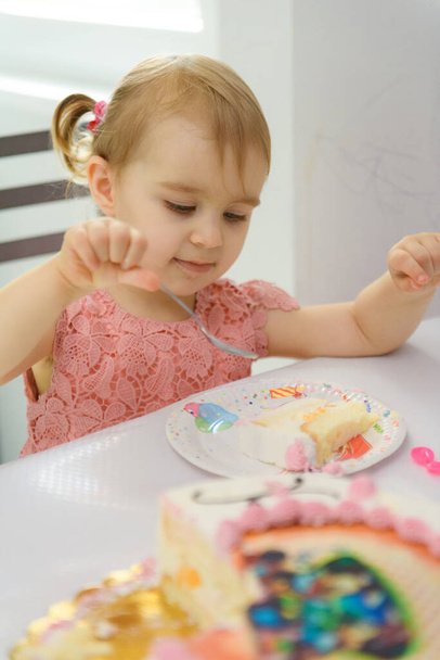 Baby meisje 1 jaar oud eten verjaardagstaart in de kamer. Verjaardagspartij. Kindertijd - Foto, afbeelding