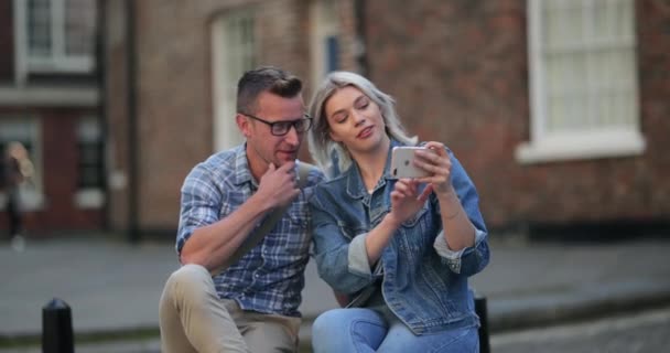 A woman showing a man something on her mobile phone while sitting on a bench. - Filmmaterial, Video