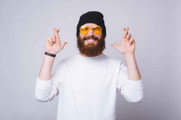 Фото модного бородатого мужчины, скрещивающего пальцы и мечтающего
 - Фото, изображение