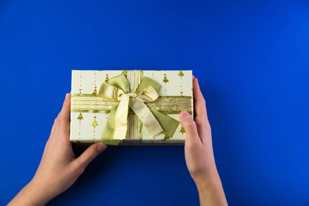 waiting for a gift, a gift box with a bow in the hands of a child on a bright blue background with a copy of the space - Foto, Imagem