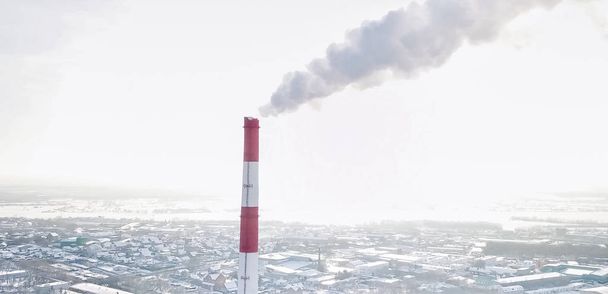 egy hőerőmű füstölgő kéménye a téli város hátterében. - Fotó, kép