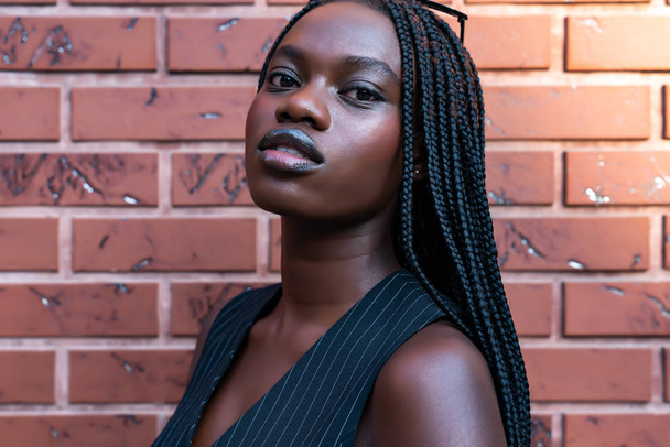 Close up portrait of the attractive afroamerican girl in black striped vest isolated over red brick wall - Photo, Image