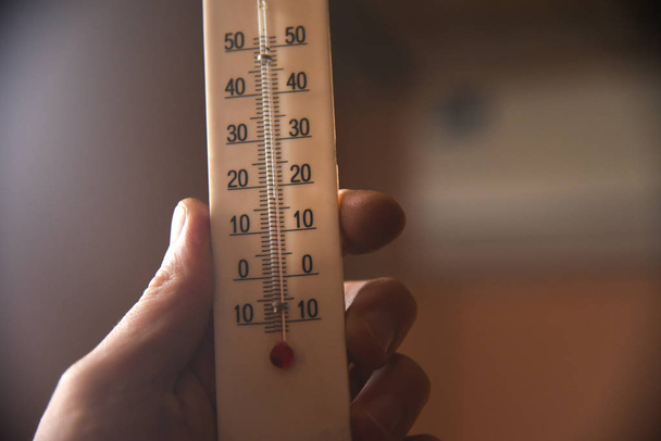 hand with a white plastic mercury thermometer shows the temperature in the room. measuring device - 写真・画像