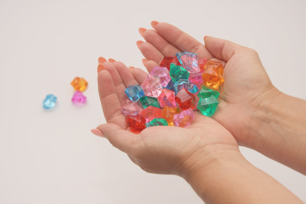 Las manos femeninas agarradas sostienen guijarros de vidrio multicolores sobre un fondo claro. Joyería y juguetes para mujeres y niños
. - Foto, Imagen