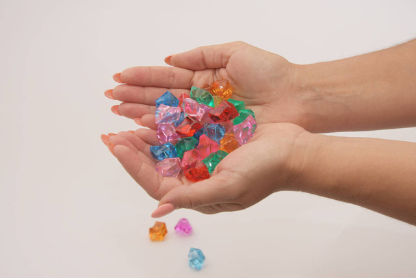 Las manos femeninas agarradas sostienen guijarros de vidrio multicolores sobre un fondo claro. Joyería y juguetes para mujeres y niños
. - Foto, imagen