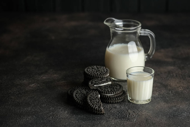 Γάλα σε κανάτα και μπισκότα σοκολάτας σε σκούρο φόντο αντίγραφο χώρου. - Φωτογραφία, εικόνα