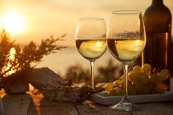 δύο ποτήρια με κρασί και μπουκάλι κατά τη διάρκεια του ηλιοβασιλέματος - Φωτογραφία, εικόνα
