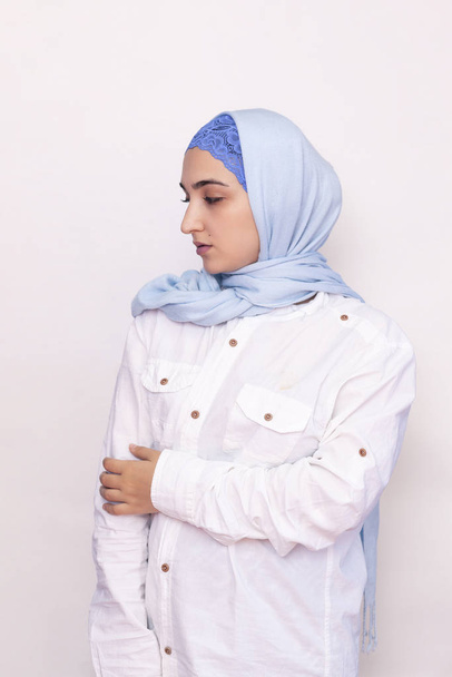 白のシャツと明るい青のヒジャーブのエレガントなイスラム教徒の女性。イスラム教徒の服でスタイリッシュなイランの女の子。魅力的な中東の女性の孤立した肖像画 - 写真・画像