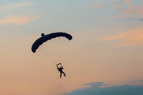 Parachutist falling from the sky in evening sunset dramatic sky. Recreational sport, Paratrooper silhouette on colored sky. - Foto, Imagen