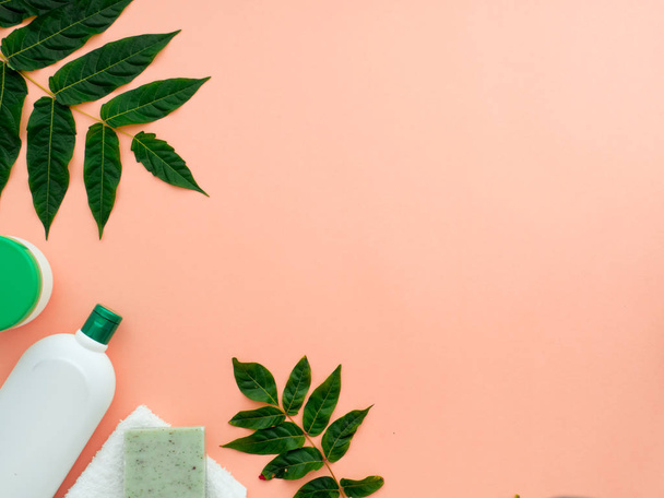 Fresh green leaves, natural cosmetics, body shower gel, liquid handmade soap and body lotion, towel isolated on a pastel orange color background. Flat lay, top view, copy space - 写真・画像