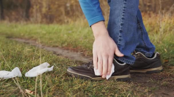 Menselijke vervuiling natuur concept. Een close-up van een onverantwoordelijke man in jeans veegt zijn schoenen af met natte doekjes en gooit het op het gras. - Video