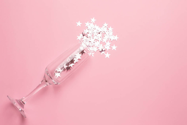 Šampaňské sklo se stříbrnými hvězdami konfety na růžovém barevném papíru pozadí minimální styl - Fotografie, Obrázek