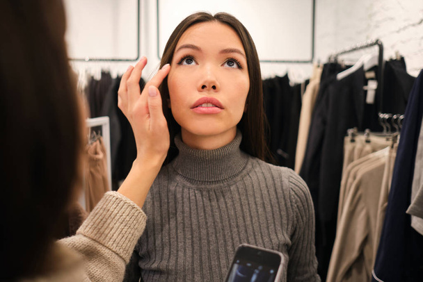 Портрет красивой азиатской стильной девушки на примерке в современном магазине моды
 - Фото, изображение