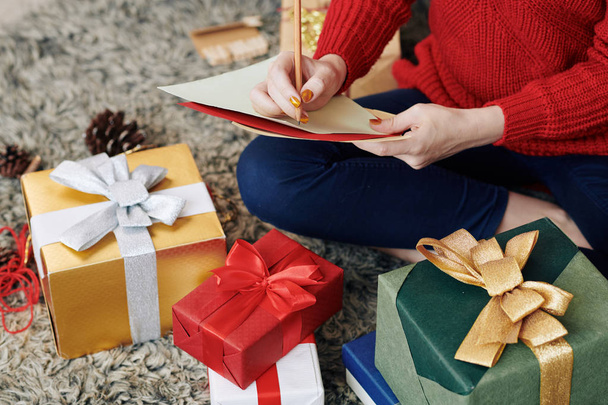 abgeschnittenes Bild einer jungen Frau, die eine Liste von Geschenken für ihre Familienmitglieder schreibt - Foto, Bild