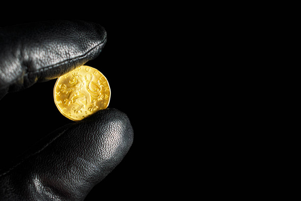 Человек в перчатке держит жёлтую монету. Чешская монета в мужской руке
 - Фото, изображение