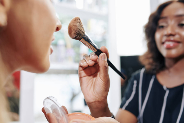 Lähikuva kuva meikki taiteilija soveltamalla jauhe pronssi posket asiakkaan pehmeä pörröinen harja
 - Valokuva, kuva