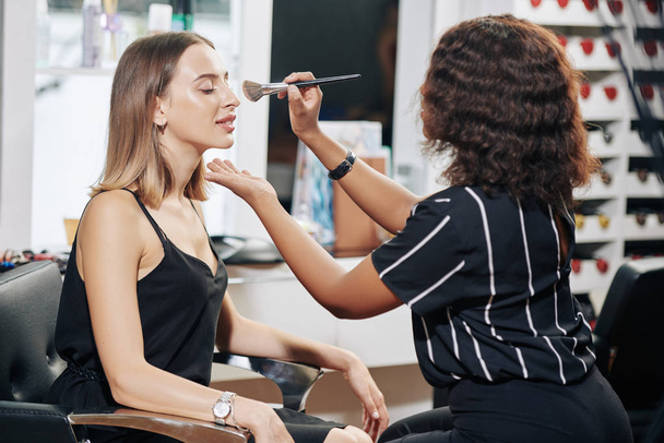 Professional make-up artist applying finishing loose face powder with fluffy blush - Фото, зображення