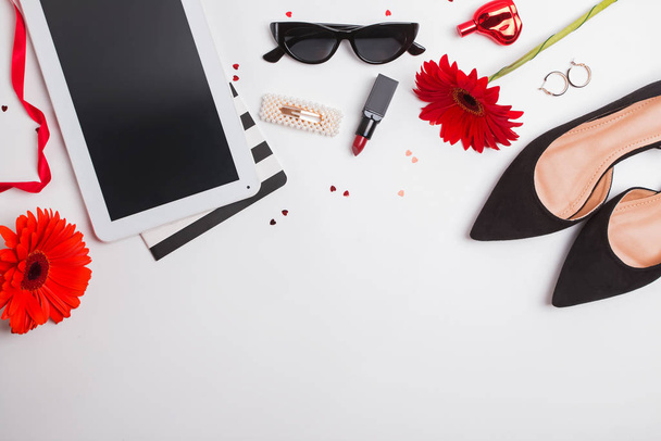 Zapatos, lápiz labial, tabletas y flores rojas sobre fondo blanco, diseño creativo plano
. - Foto, imagen