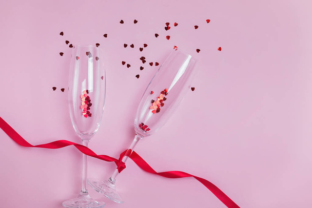 Two champagne glasses, red ribbon and heart shaped confetti splashes. - Photo, image