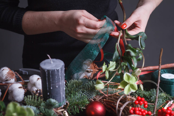Gros plan d'une fleuriste faisant une couronne de Noël de branches de sapin, bulles de Noël et décor naturel, mise au point sélective
 - Photo, image