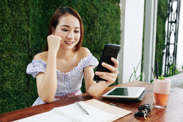 Mulher asiática bonita ler mensagens de texto engraçadas de seu amigo quando tendo coquetel no café
 - Foto, Imagem