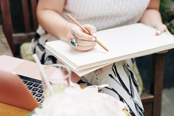Imagen de primer plano del logotipo del dibujo de la mujer de negocios o boceto con lápiz en su cuaderno de dibujo cuando se sienta al aire libre en la mesa
 - Foto, imagen