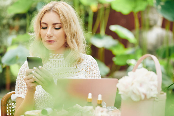 Красива молода елегантна бізнес-леді сидить на відкритому повітрі і читає текстові повідомлення в її смартфоні
 - Фото, зображення