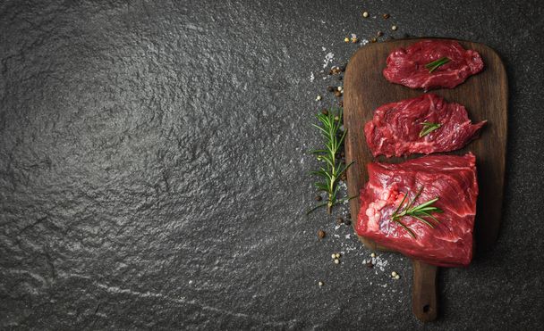 Rauwe biefstuk met kruiden en specerijen rozemarijn / Vers vlees rundvlees gesneden op houten snijplank achtergrond - Foto, afbeelding