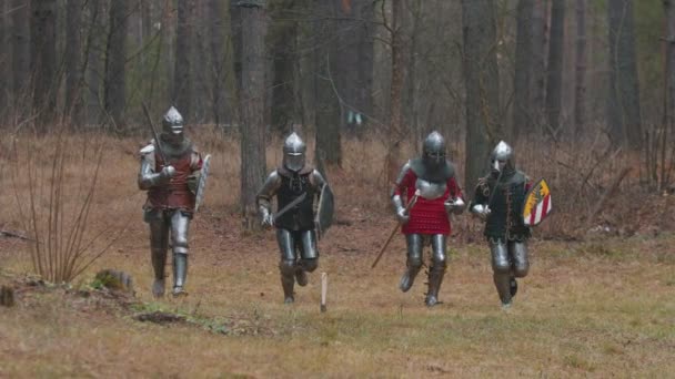 Τέσσερις άνδρες ιππότες τρέχουν στη σειρά στο δάσος με πλήρη θωράκιση κρατώντας όπλα - Πλάνα, βίντεο