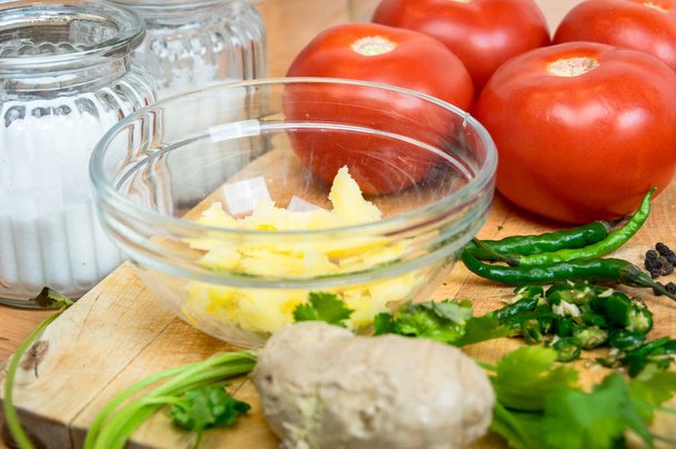 Uma tigela de vidro com manteiga clarificada cercada por legumes e especiarias, tomates vermelhos, pimenta, gengibre - Foto, Imagem