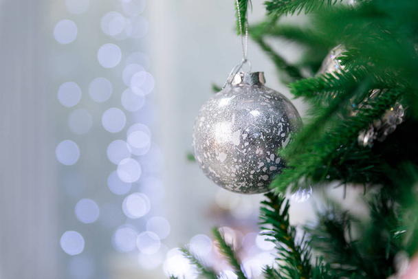 Close up of beautiful christmas decoration- bauble Christmas silver ball hanging on the Christmas green tree on the background of bokeh. Silver Christmas winter background. Selective focus - Foto, Imagen