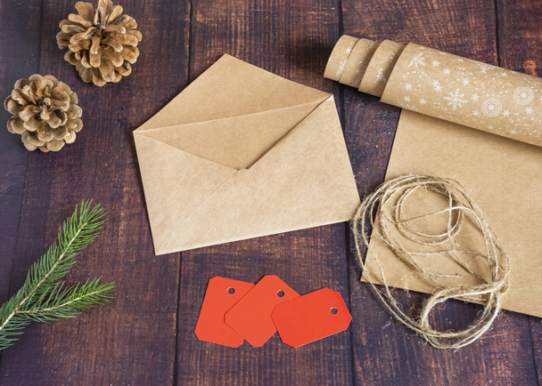 Gift bag made of handmade kraft paper on a wooden background in a Christmas style, decorated with Christmas tree balls, cones, a ball of rope, fir branches. Christmas, New Year, winter holiday. - Foto, imagen