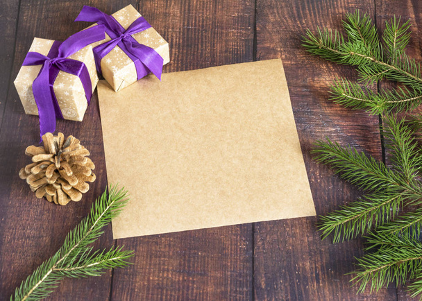 Τσάντα δώρου από χειροποίητο χαρτί κραφτ σε ξύλινο φόντο σε χριστουγεννιάτικο στυλ, διακοσμημένη με μπάλες χριστουγεννιάτικου δέντρου, κώνους, μια μπάλα σχοινιού, κλαδιά ελάτης. Χριστούγεννα, Πρωτοχρονιά, χειμερινές διακοπές. - Φωτογραφία, εικόνα