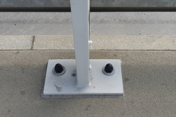 Gray iron strut road chipper bolted to the ground. Connection of the road fence with the ground with strong iron bolts with plastic covers. Road safety. - Φωτογραφία, εικόνα