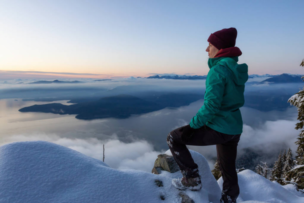 Adventurous Blond Caucasian Girl sitting on top of a snow covered mountain during a colorful winter sunset. Taken on St Mark's Summit, North of Vancouver, BC, Canada. - 写真・画像