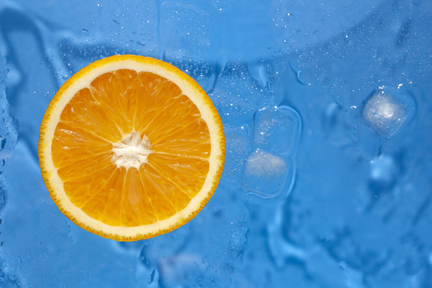 青の背景にオレンジと氷のキューブのスライス - 写真・画像