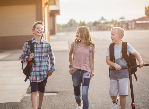 Freimütiges Foto einer Gruppe lächelnder Grundschüler auf dem Schulhof nach der Schule. Zurück zum Schulkonzept. Echte Kinder laufen von der Schule nach Hause und haben Spaß - Foto, Bild