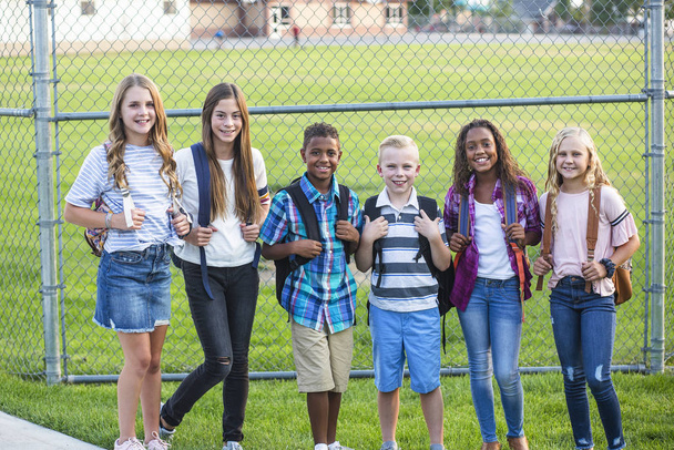 Grupa uczniów uśmiechających się stojąc razem na szkolnym placu zabaw. Powrót do zdjęcia szkolnego - Zdjęcie, obraz