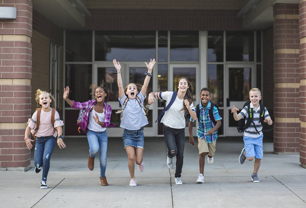 Groepsschoolkinderen rennen als ze het schoolgebouw verlaten Terug naar schoolfoto van een divers groepje kinderen in rugzakken en klaar om van school naar huis te gaan - Foto, afbeelding