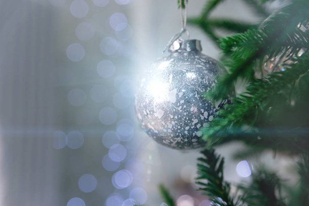 Close up of beautiful christmas decoration - bauble Christmas silver ball hanging on the Christmas tree on the background of blue bokeh. Christmas winter background with bokeh and magic highlights. - Zdjęcie, obraz
