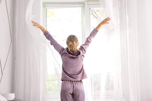 Morning of beautiful young woman opening curtains in bedroom - Foto, Bild