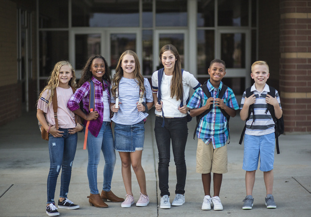 Retrato grupal de niños en edad preescolar sonriendo frente al edificio escolar. Volver a la foto escolar de un grupo diverso de niños con mochilas y listos para ir a la escuela. - Foto, Imagen