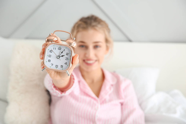 Morning of beautiful young woman with alarm clock in bed - Photo, image