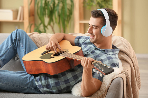Pohledný muž s kytarou poslouchající doma hudbu - Fotografie, Obrázek