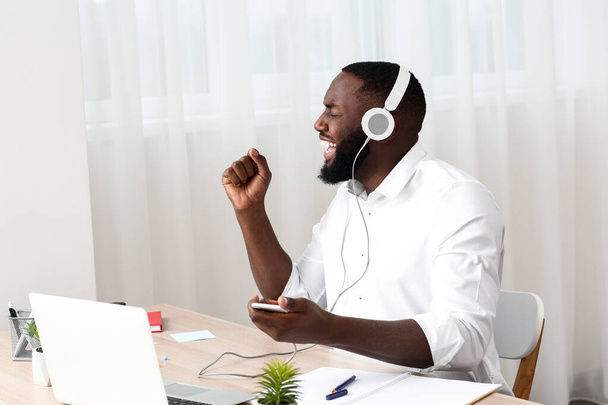 Emotionele Afro-Amerikaanse man luistert naar muziek in het kantoor - Foto, afbeelding