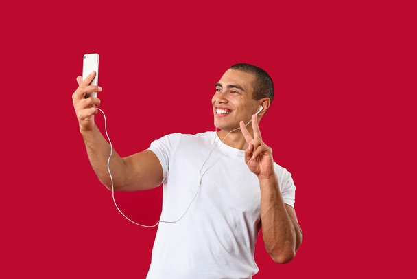 Portrait of handsome young man listening to music and taking selfie on color background - Photo, Image