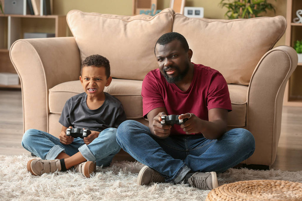 Portrait of emotional African-American man and his little son playing video game at home - Photo, Image